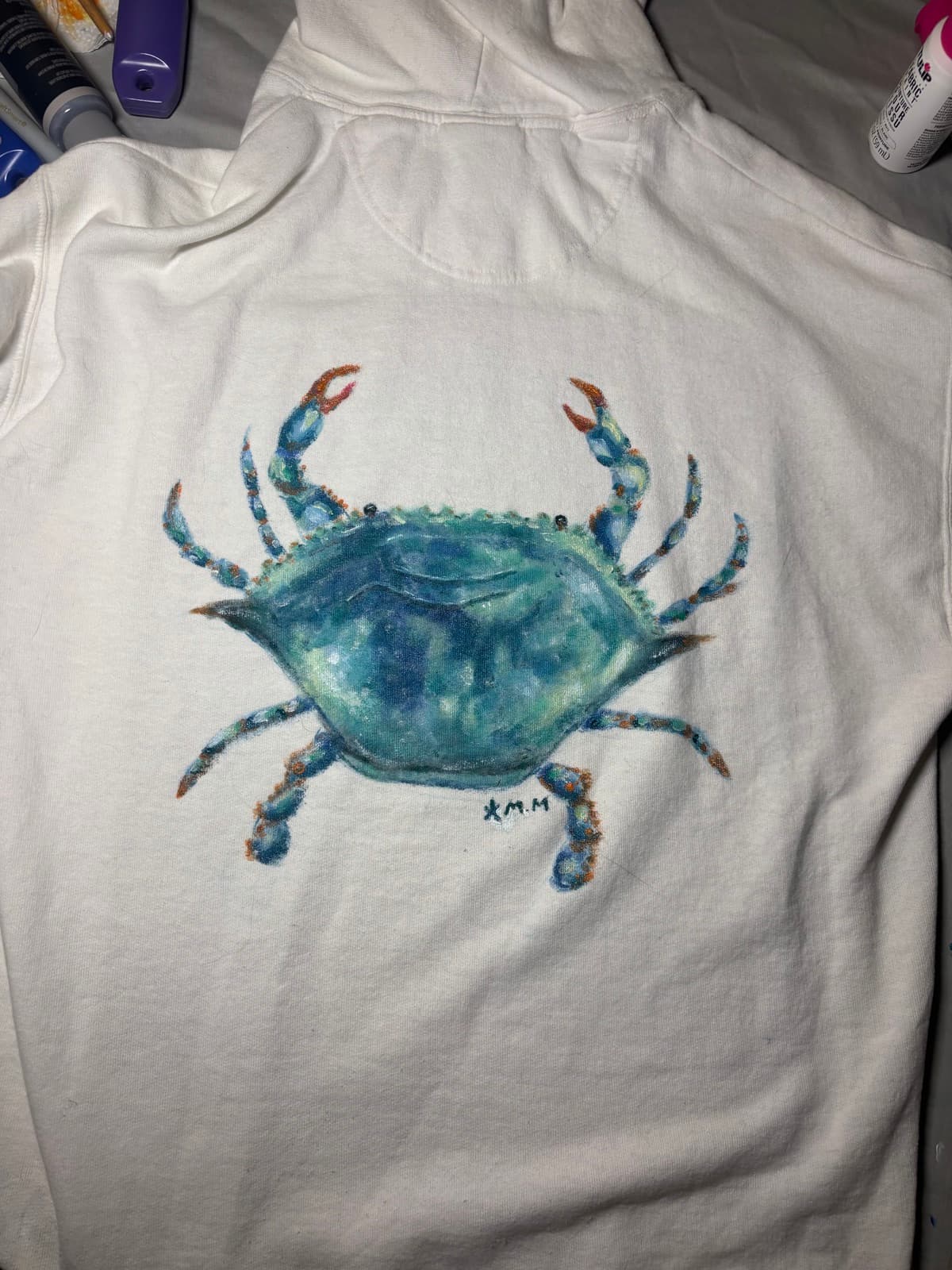 Hand-painted blue crab design, back view, on a custom sweatshirt by Madeleine MacNutt